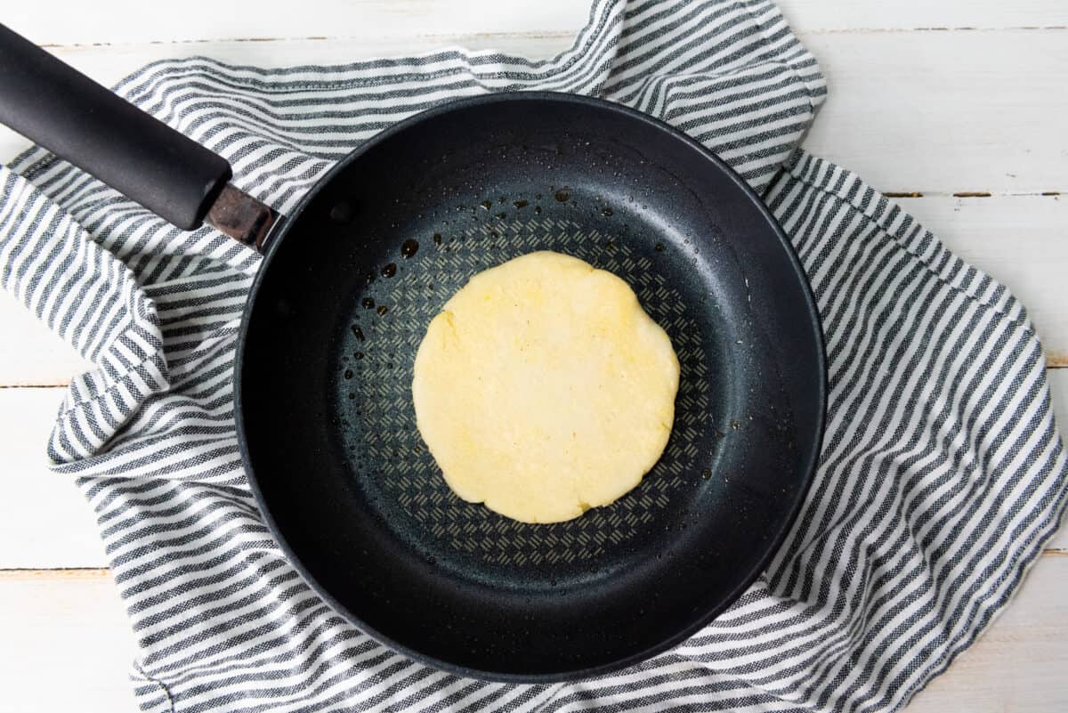 Golden-brown arepa frying in a skillet