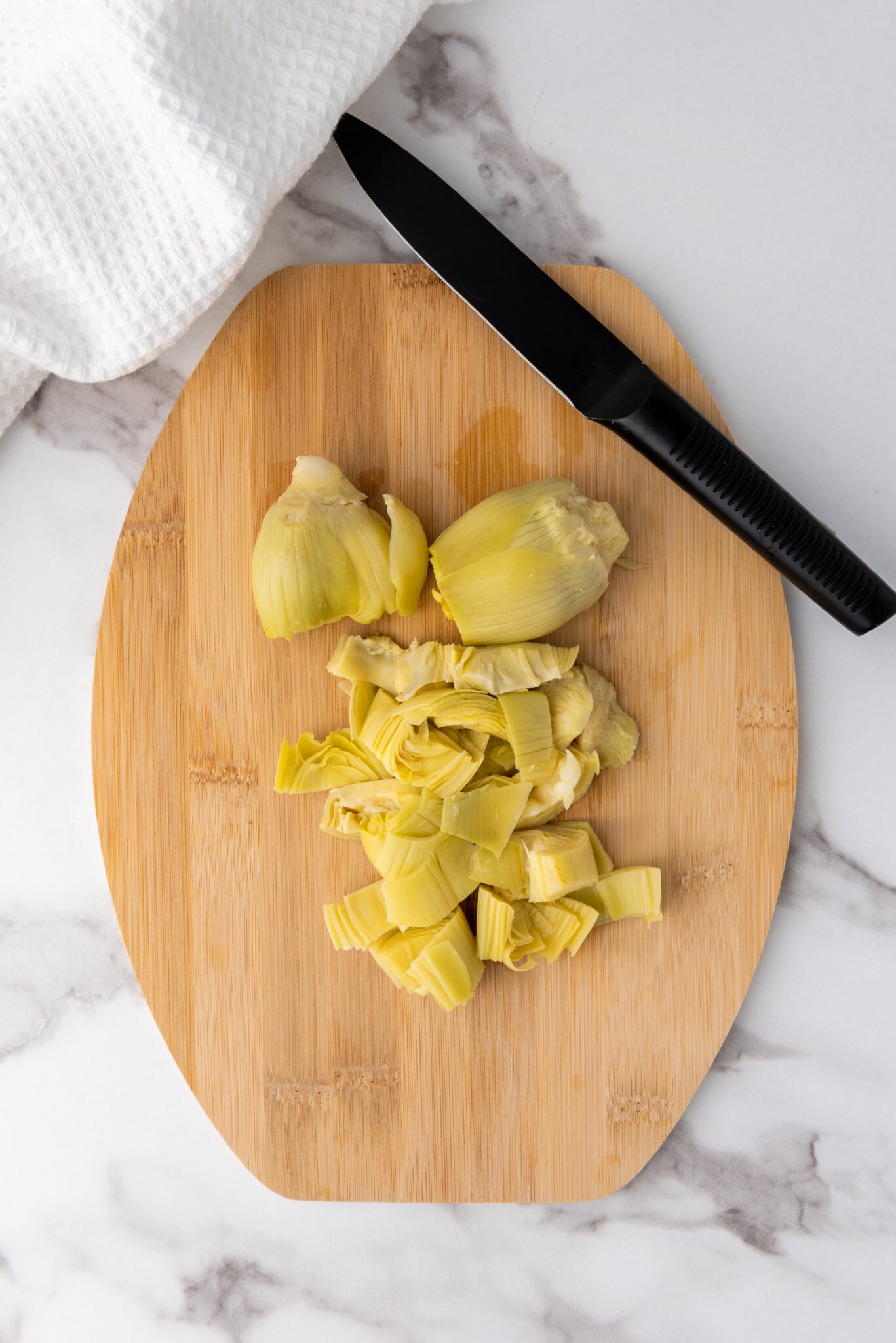 Fresh artichoke hearts being finely chopped on a wooden cutting board.
