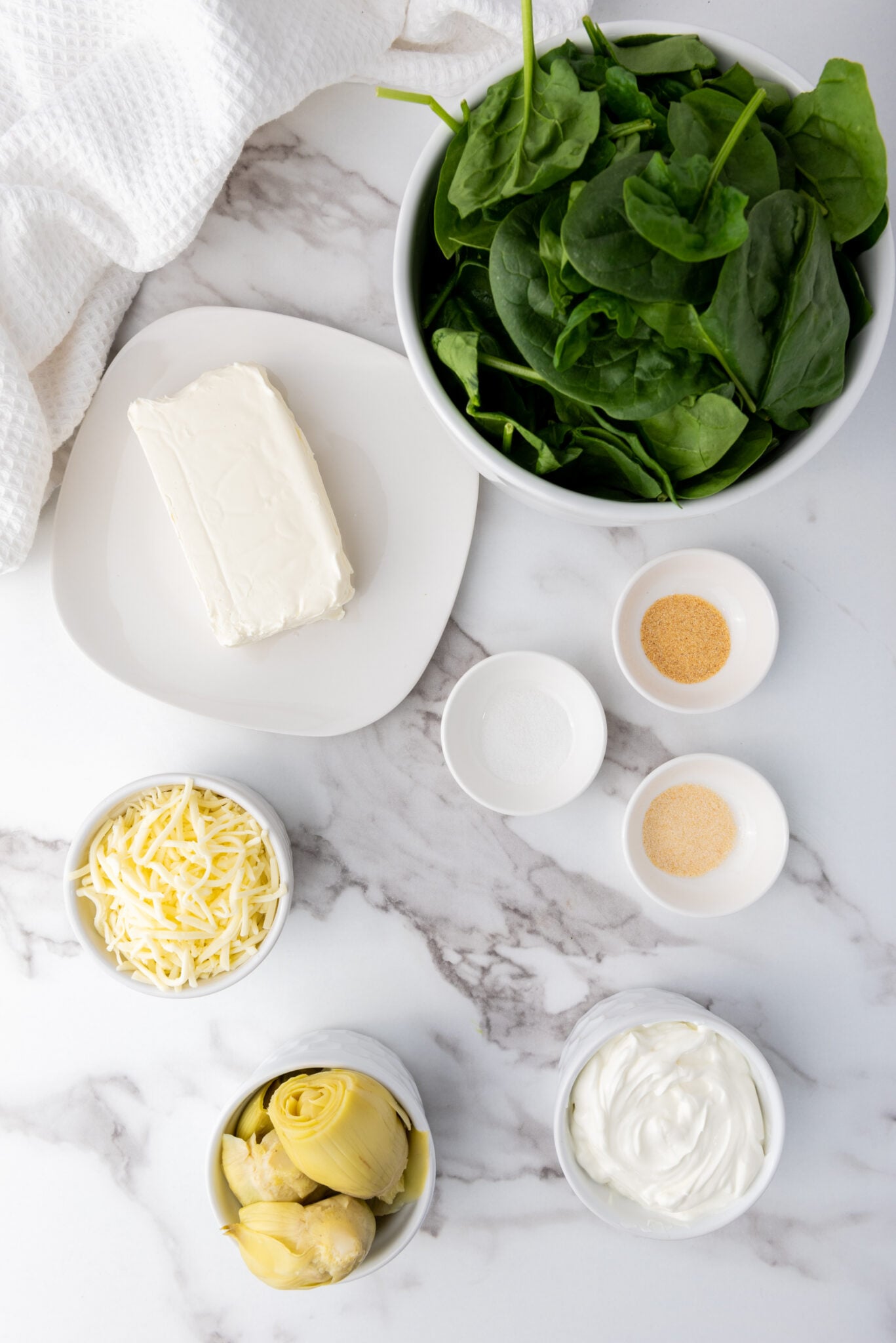 Ingredients for a spinach artichoke dip recipe arranged on a marble surface.