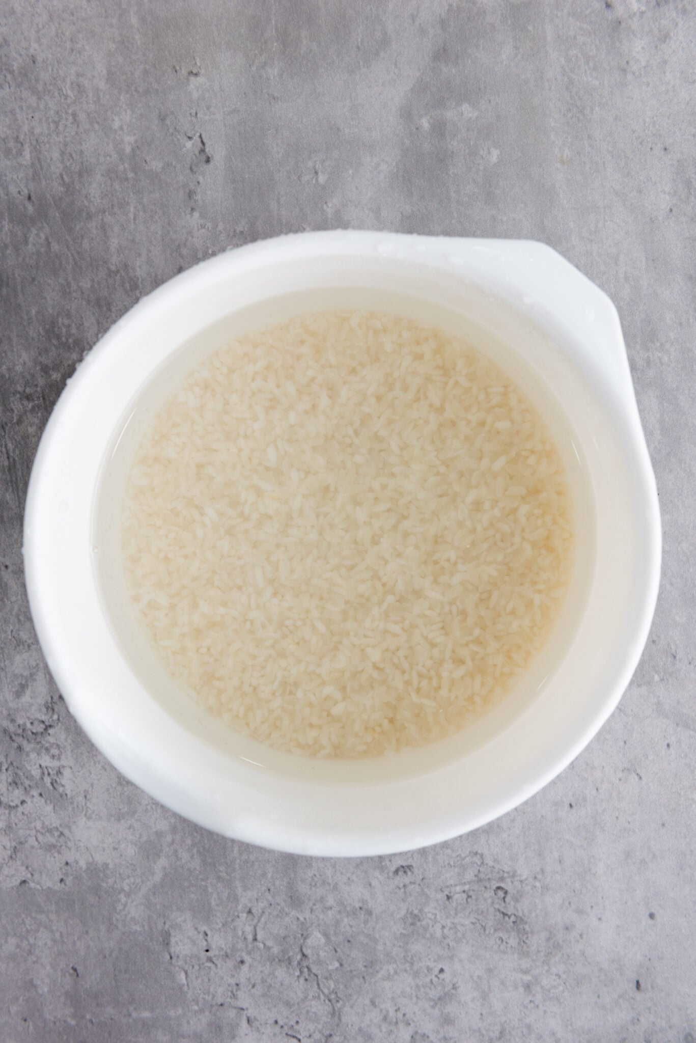 Hand rinsing sushi rice under cold tap water, clear water in bowl after multiple rinses.