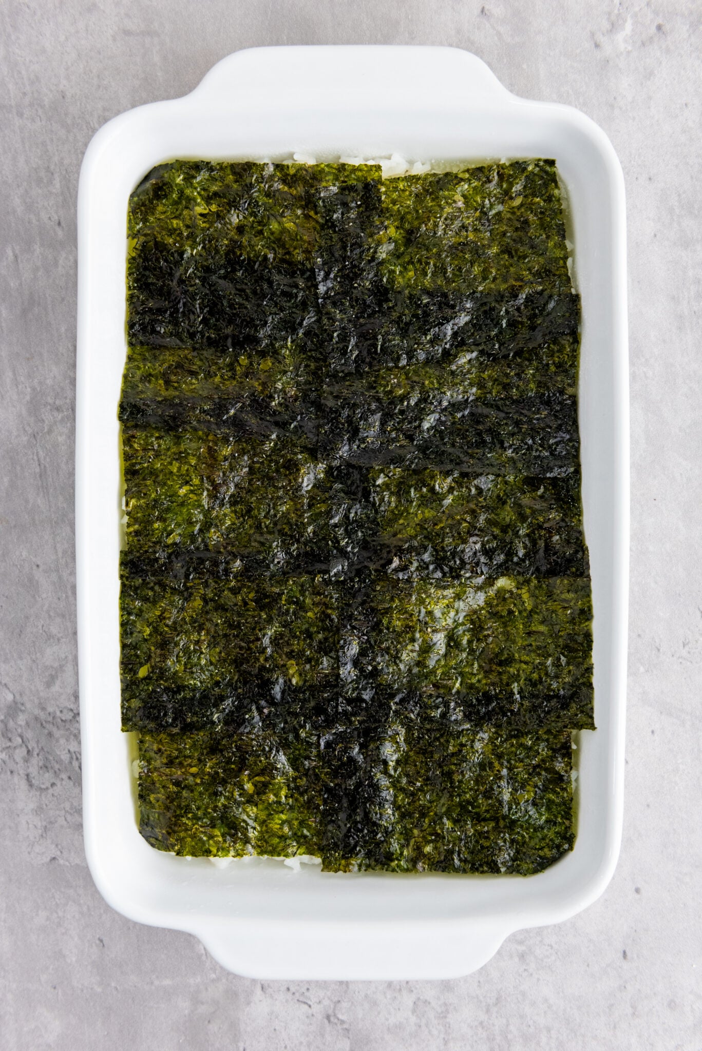 Casserole dish with sushi rice now covered with neatly laid out nori sheets.