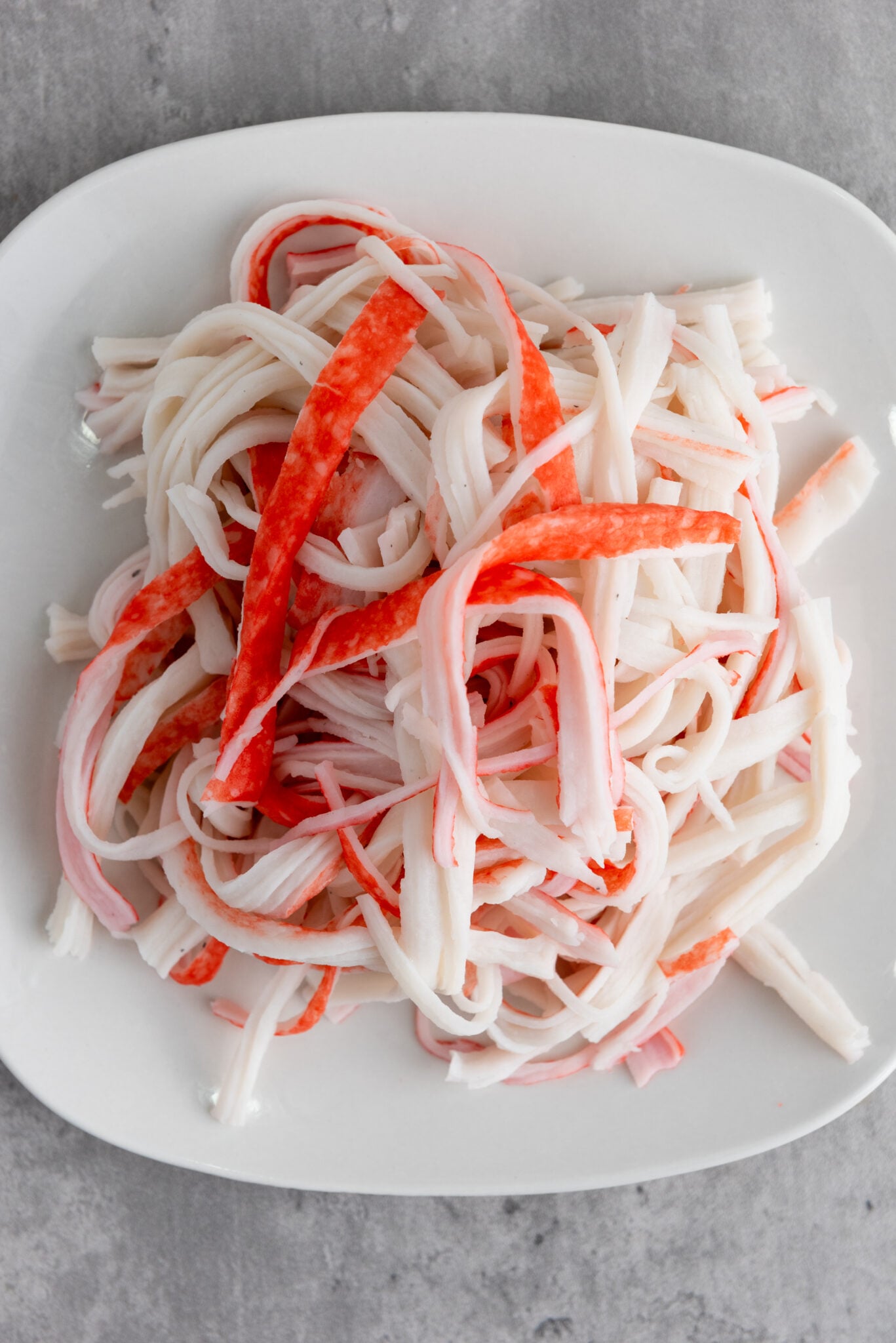 Hand-shredded pieces of imitation crab on a white bowl.