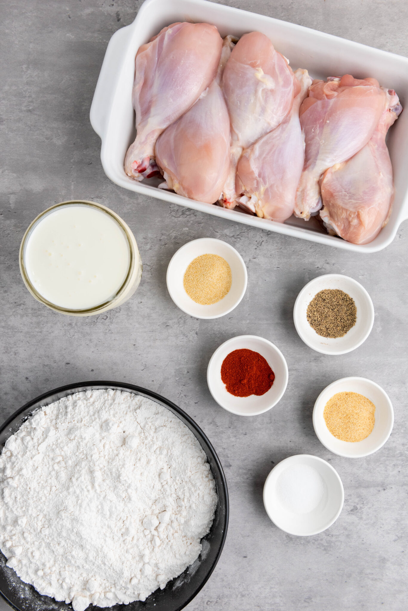 Ingredients for preparation: raw chicken breasts, flour, spices, and a bowl of buttermilk batter on a kitchen surface.