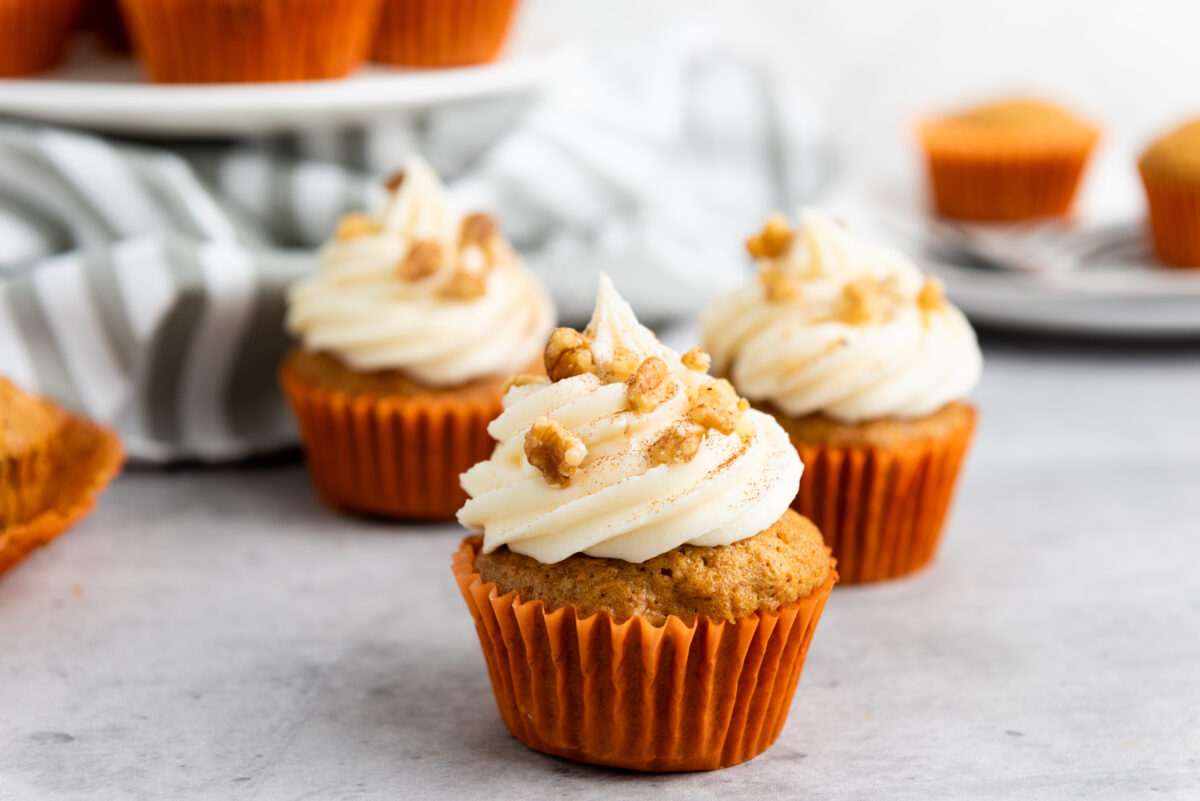 Homemade carrot cake cupcakes with cream cheese frosting and nut toppings on a kitchen counter.