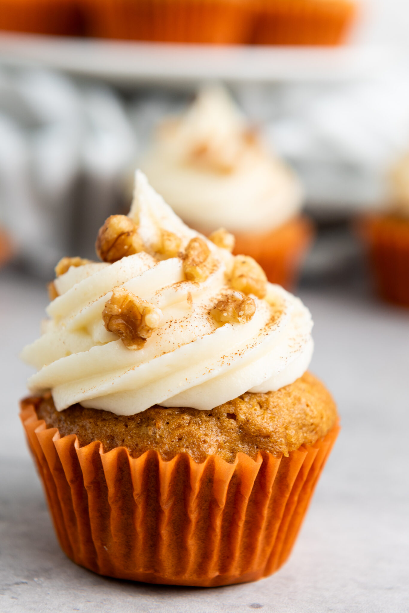 A carrot cake cupcake topped with cream cheese frosting and walnuts.