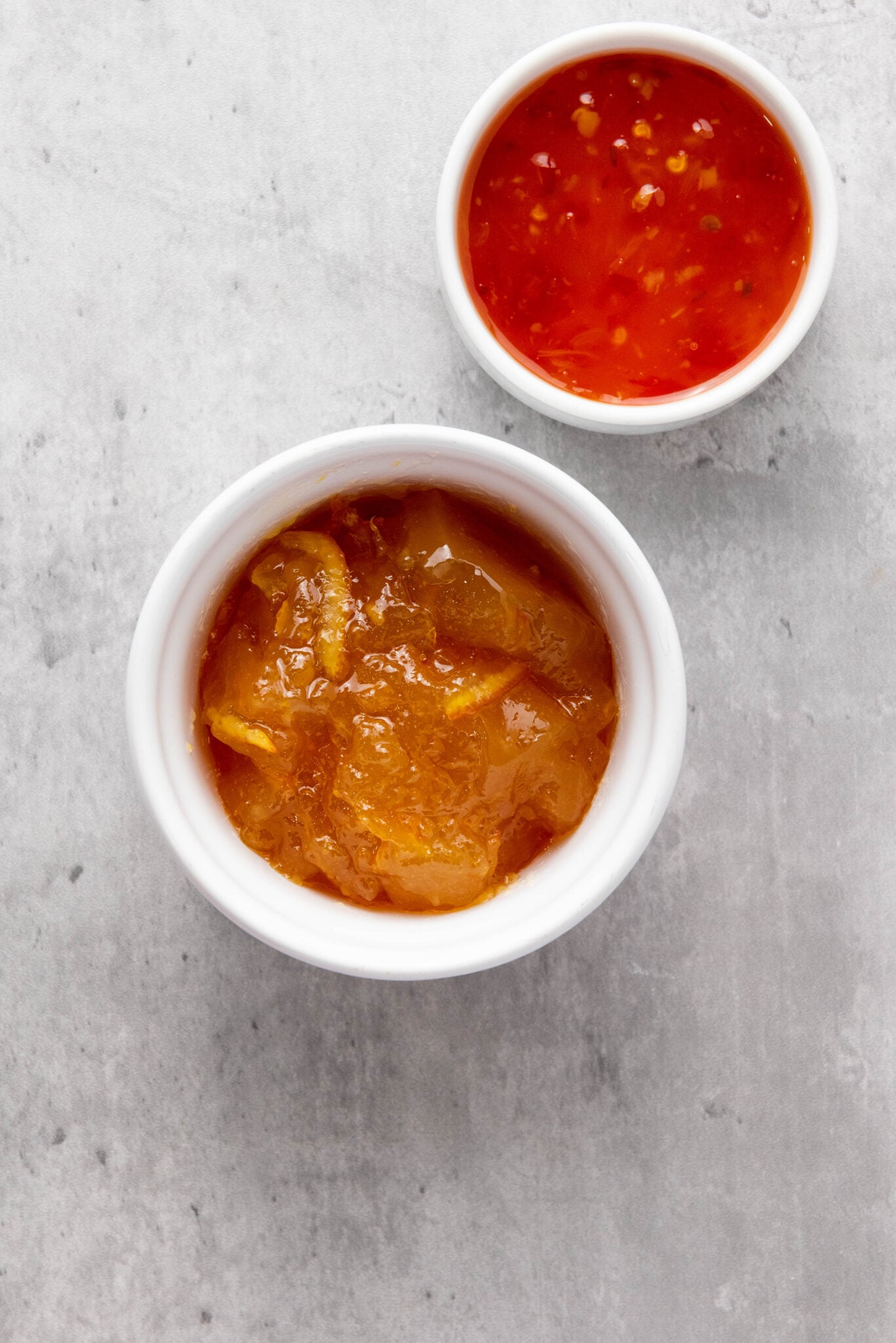 Two small bowls containing sauces on a grey surface, one with a chunky orange sauce for Outback Coconut Shrimp and the other with a red chili sauce.