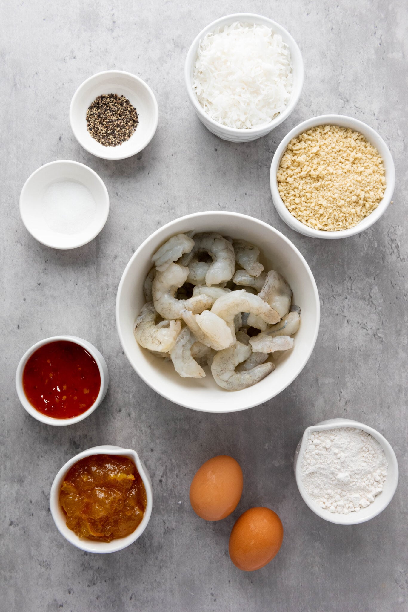Ingredients for an Outback Coconut Shrimp recipe laid out on a kitchen counter, including shrimp, eggs, flour, breadcrumbs, coconut, and seasonings.