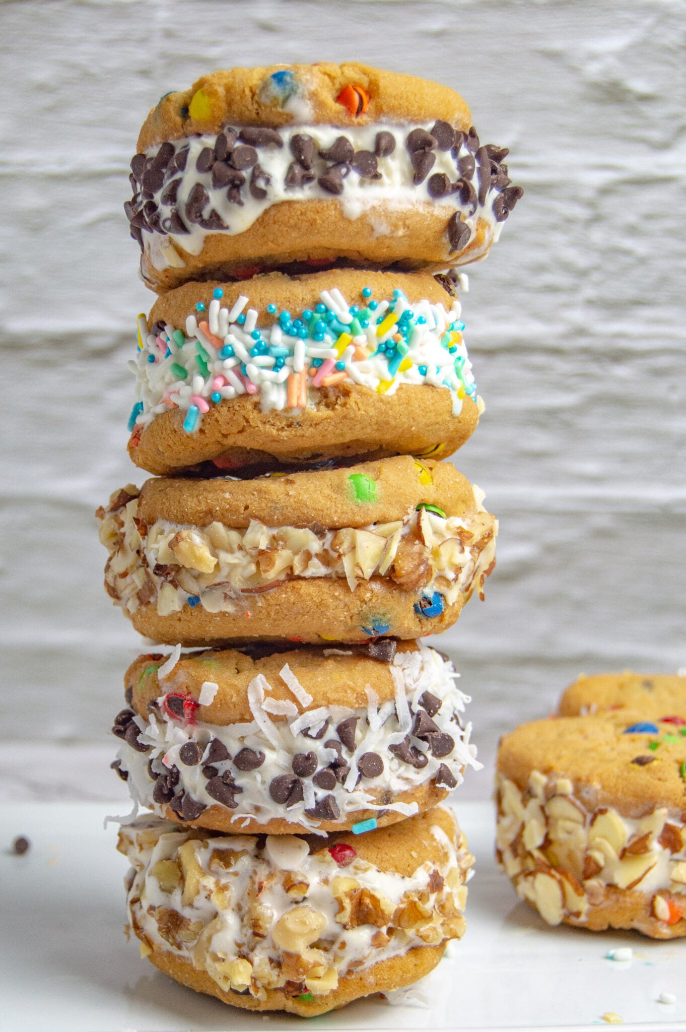 A stack of assorted decorated classic cookie ice cream sandwiches against a white background.