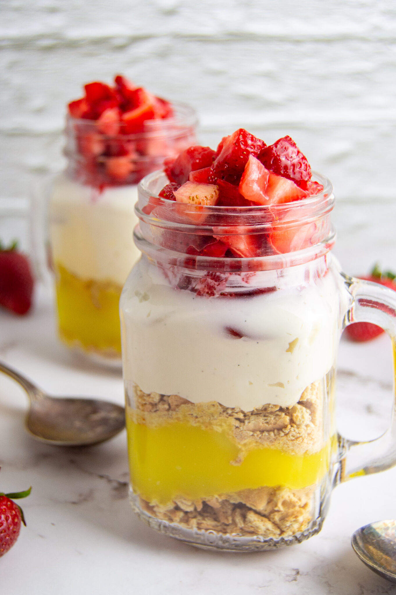 Strawberry Lemon Cheesecake parfaits with layers of crushed biscuits, lemon curd, cream cheese, and fresh strawberries served in glass jars.