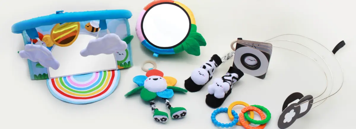 An assortment of baby toys and items, including a tambourine, mirror, plush toys, teethers, and sunglasses, displayed on a white background.
