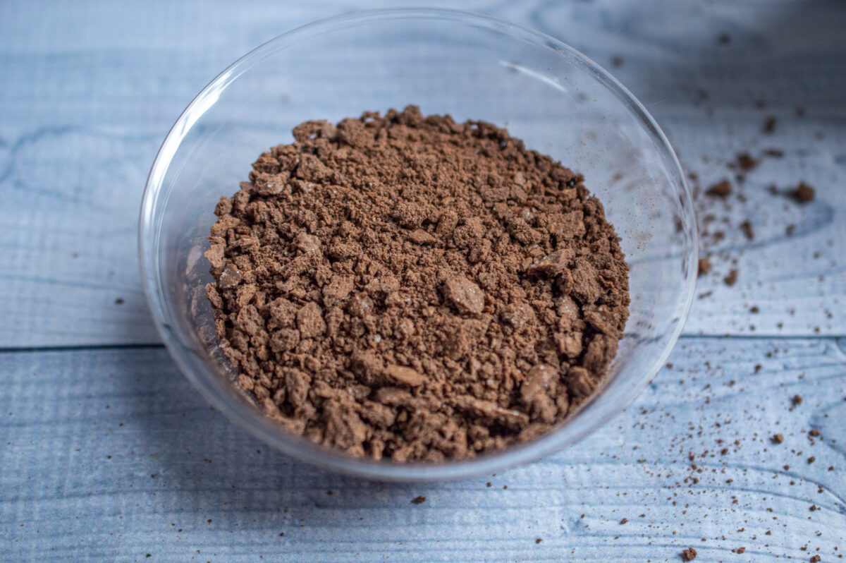 A clear glass bowl filled with crumbled No Bake Chocolate Cherry Cheesecake on a wooden surface.