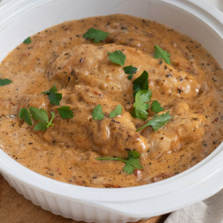 A bowl of creamy marry me chicken topped with fresh cilantro leaves, served in an white ceramic dish.
