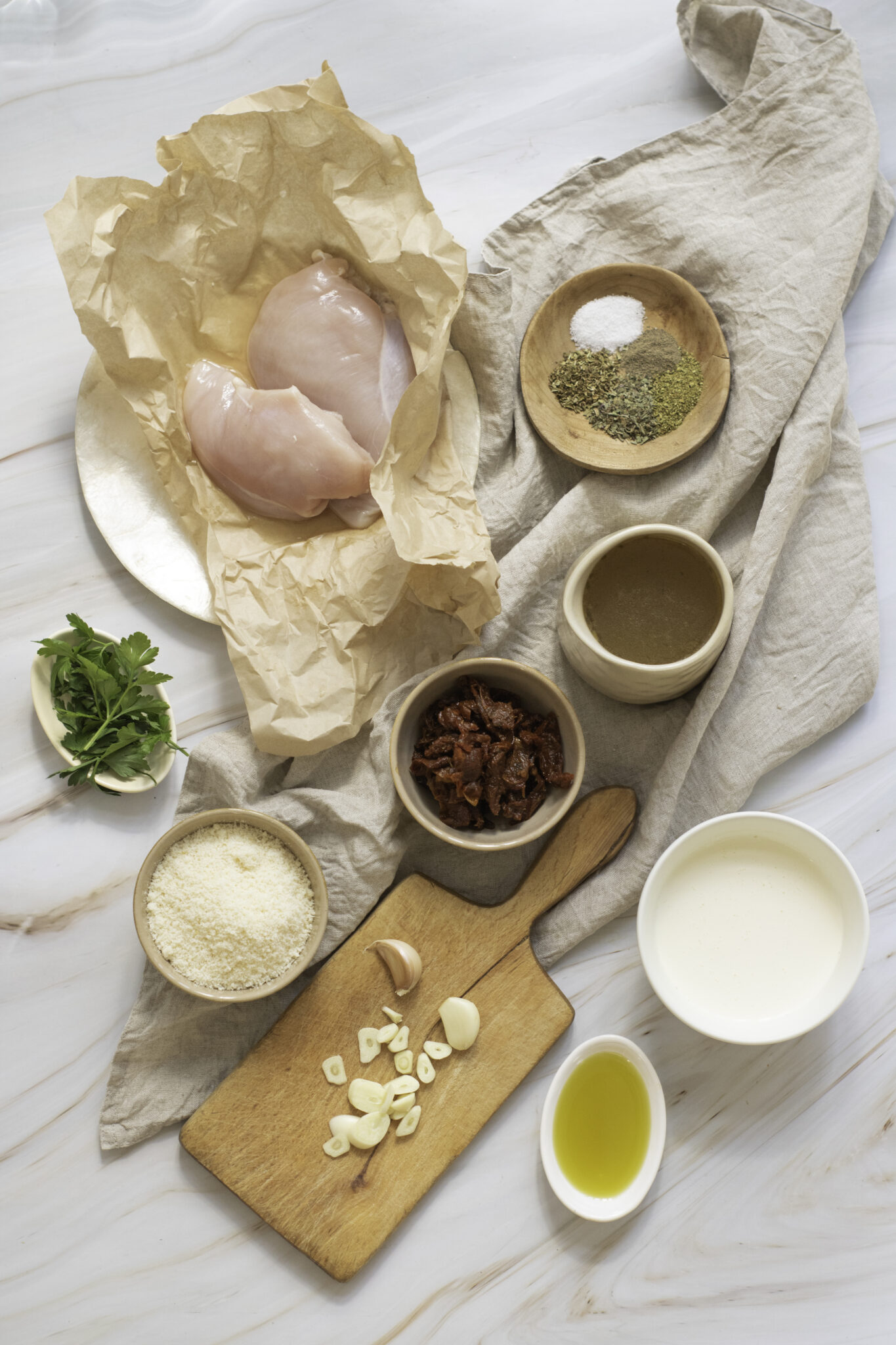 Ingredients for cooking "Marry Me Chicken" laid out on a marble surface, including chicken breast, spices, flour, garlic, oil, and milk.