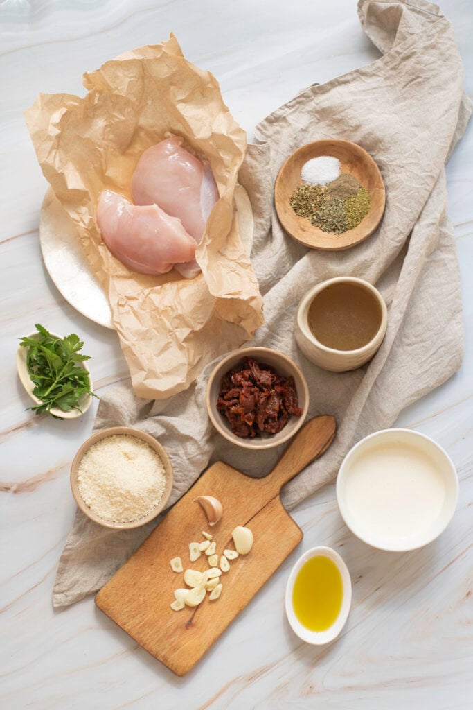 Ingredients for cooking "Marry Me Chicken" laid out on a marble surface, including chicken breast, spices, flour, garlic, oil, and milk.