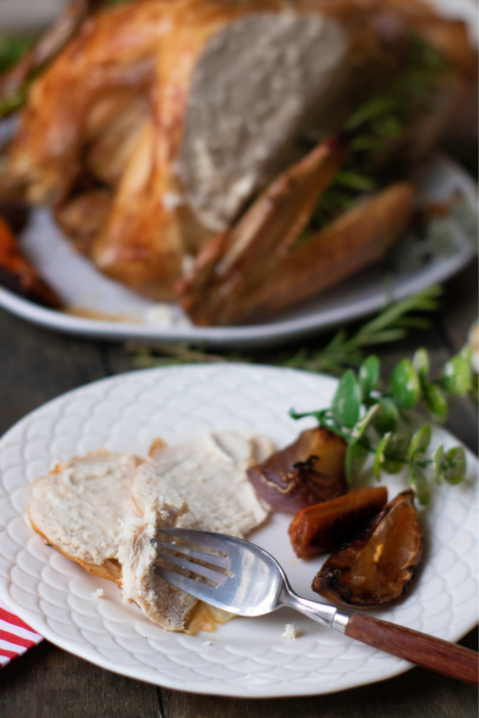 A plate with slices of roasted turkey and a fork beside roasted vegetables. An additional plate with more turkey is in the background, showcasing the best Thanksgiving recipe for your holiday feast.