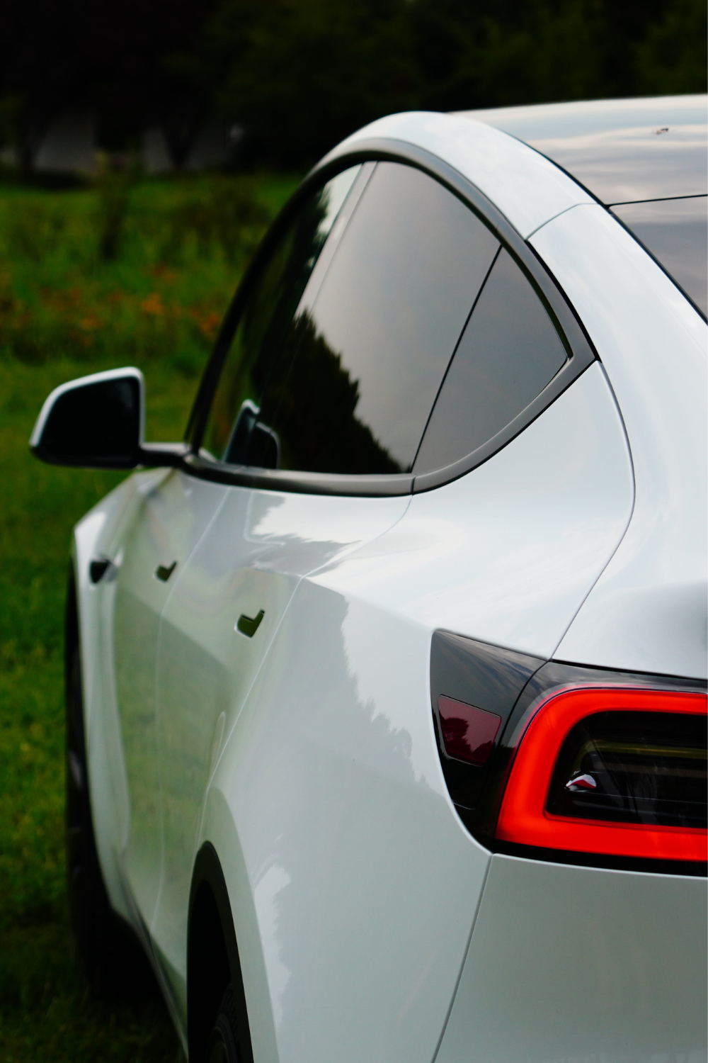 A white car with tinted windows is parked on a grassy area, showcasing the pristine white car paint on its rear side and taillight.