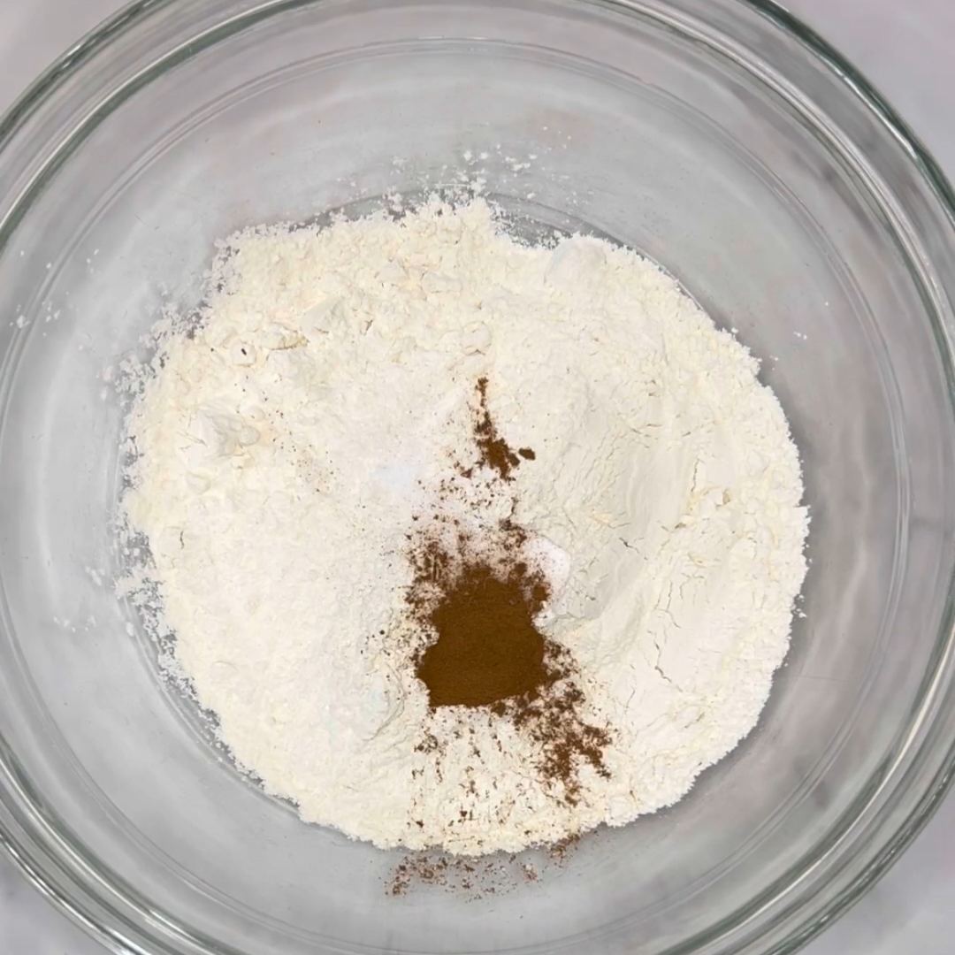 A clear glass bowl containing a mixture of flour and a small amount of ground cinnamon, perfect for whipping up easy peach muffins.
