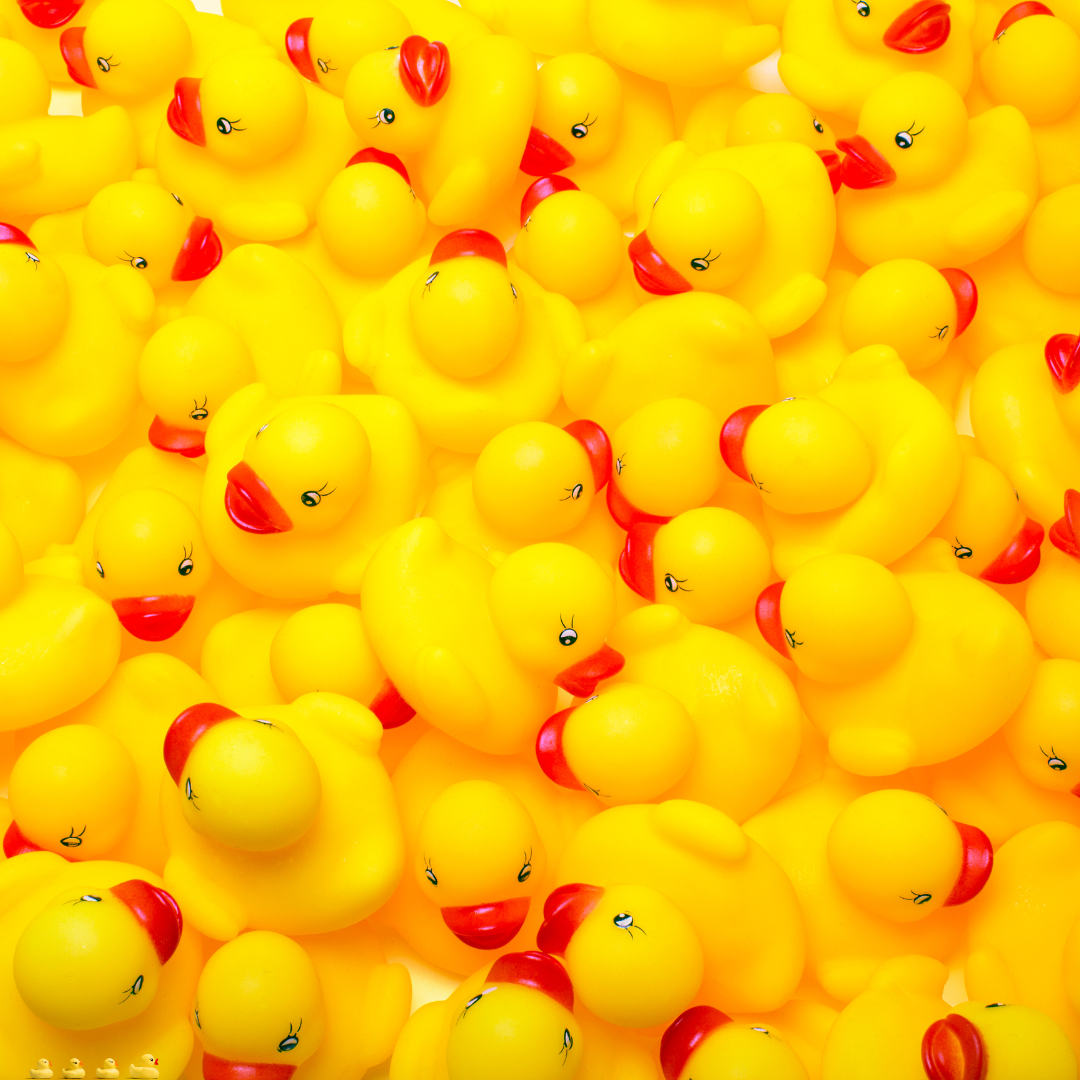 A large pile of yellow rubber ducks with red beaks and eyes is closely packed together.