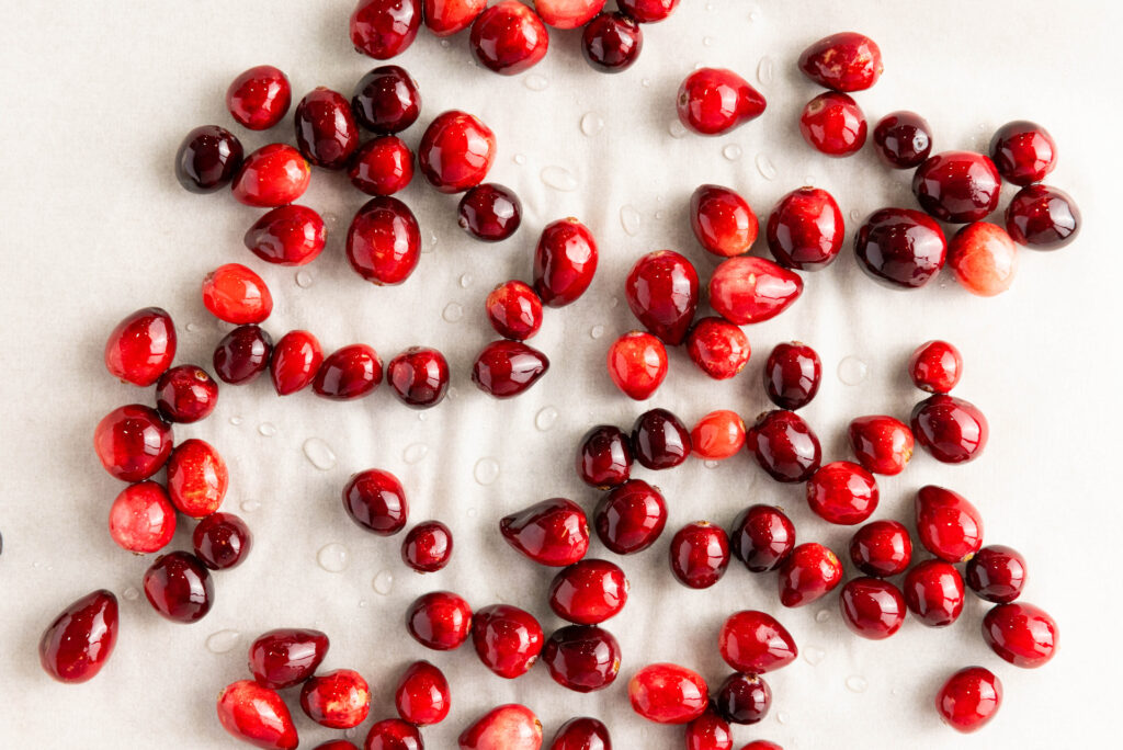 A scattering of fresh cranberries glistens with water droplets on a pristine white surface, inspiring thoughts of a delightful cranberry recipe or even the creation of sugared cranberries to sweeten your table.