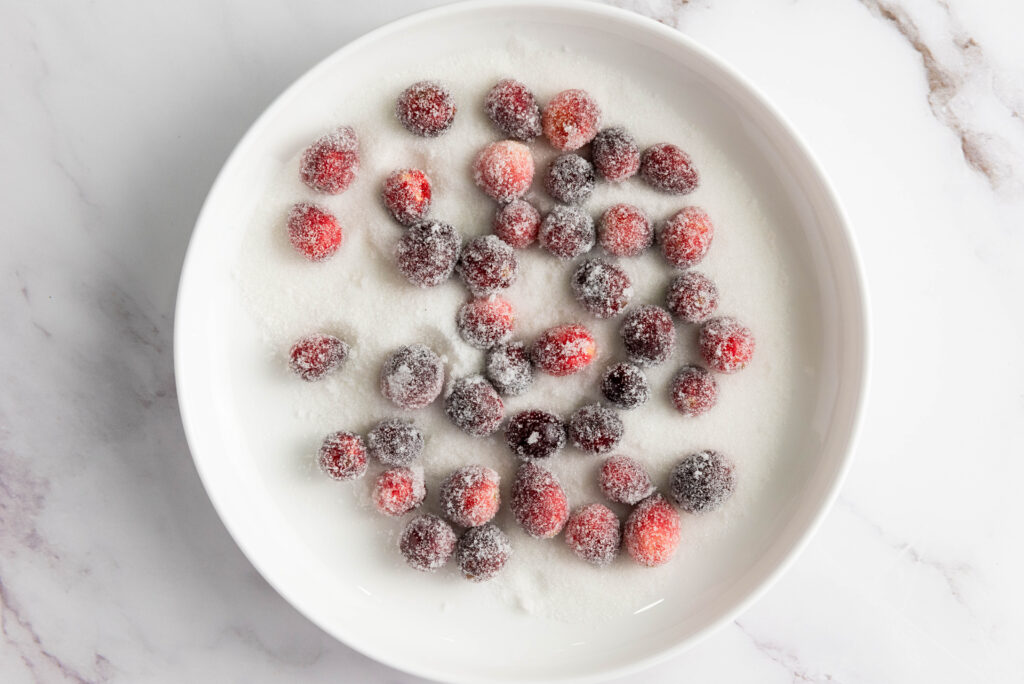 A white plate with sugared cranberries glistens on a marble surface, showcasing nature's jewelry.