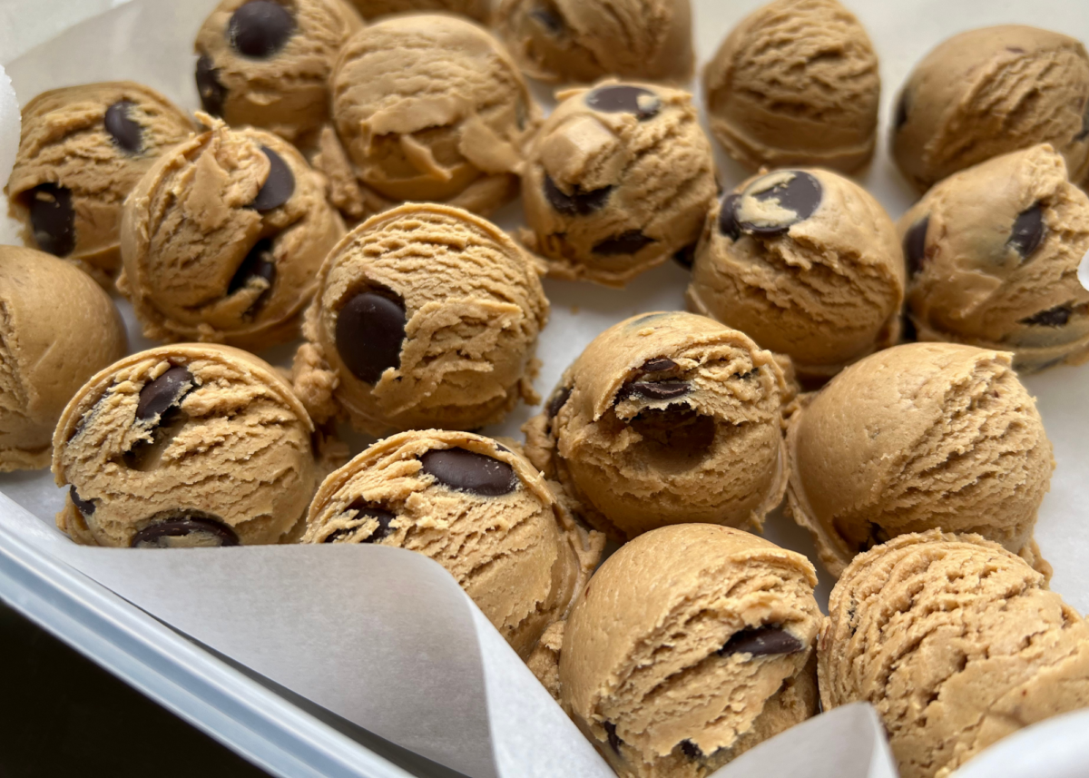 Rows of round protein bites, made from a Clean Simple Eats dough balls recipe, are arranged closely together on parchment paper in a container.