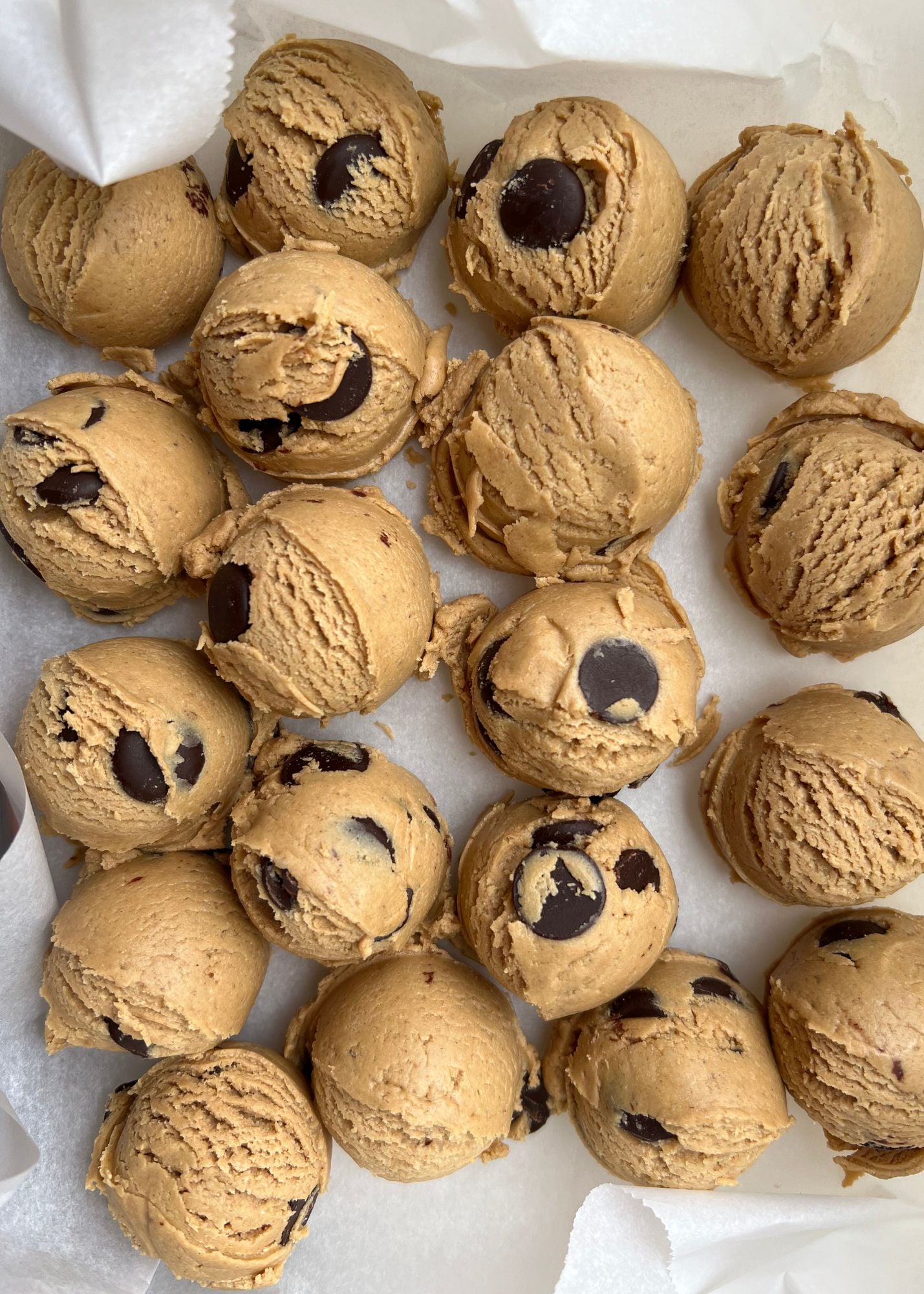 Scoops of chocolate chip cookie dough arranged closely together on a parchment-lined surface, ready for baking—perfect for trying the CSE dough balls recipe from Clean Simple Eats.