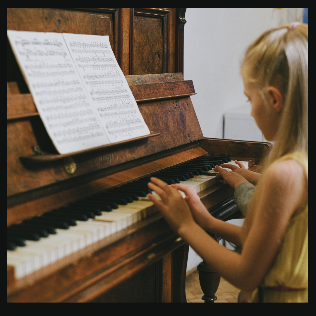 A young girl with blonde hair plays a wooden piano, her fingers dancing gracefully across the keys. Above them rests sheet music, guiding her tune as she learns through a Simply Piano free trial, opening up a world of melodies.
