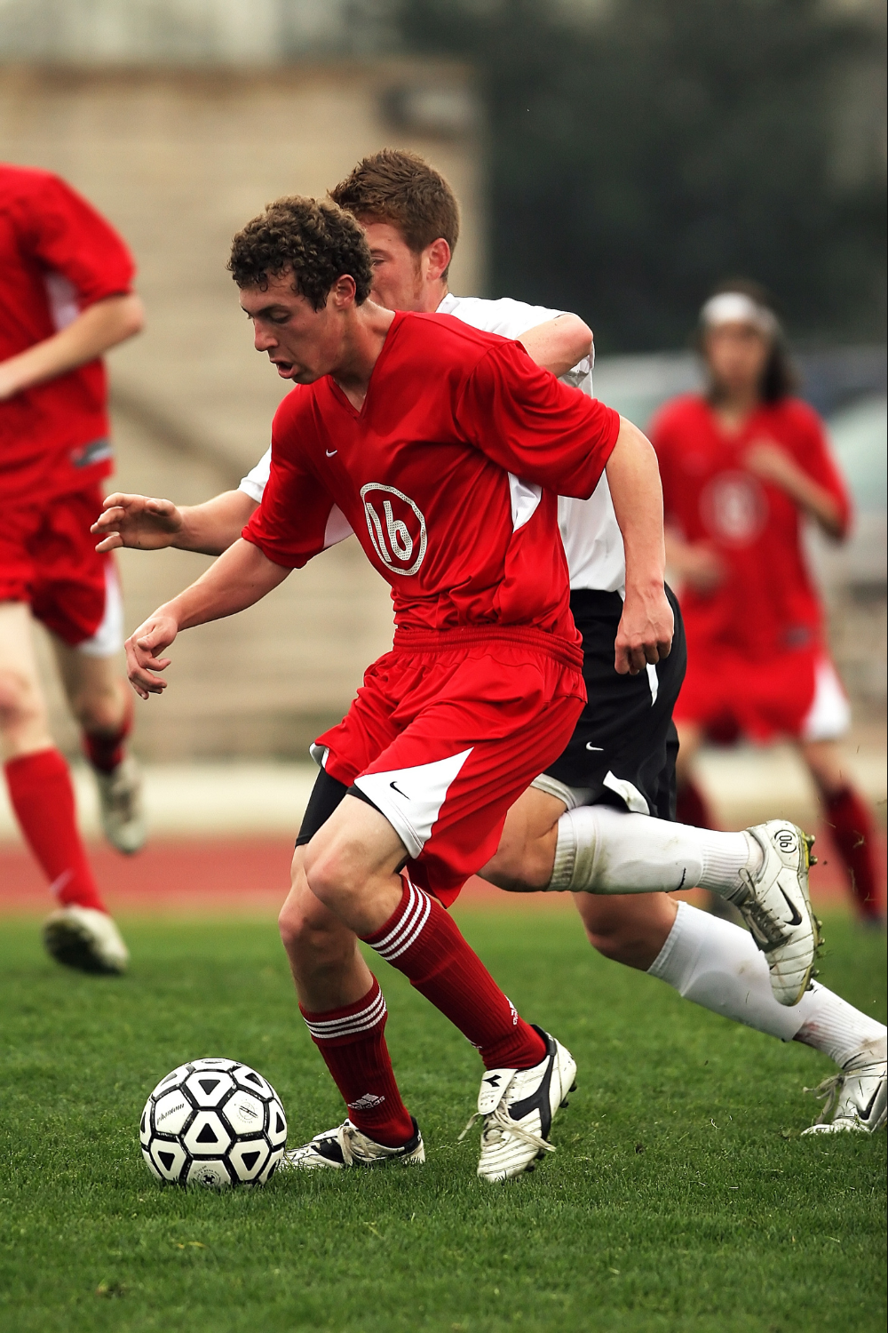 Two teen athletes in red and white jerseys compete for the ball on a grassy field, showcasing their skills with grace and agility.