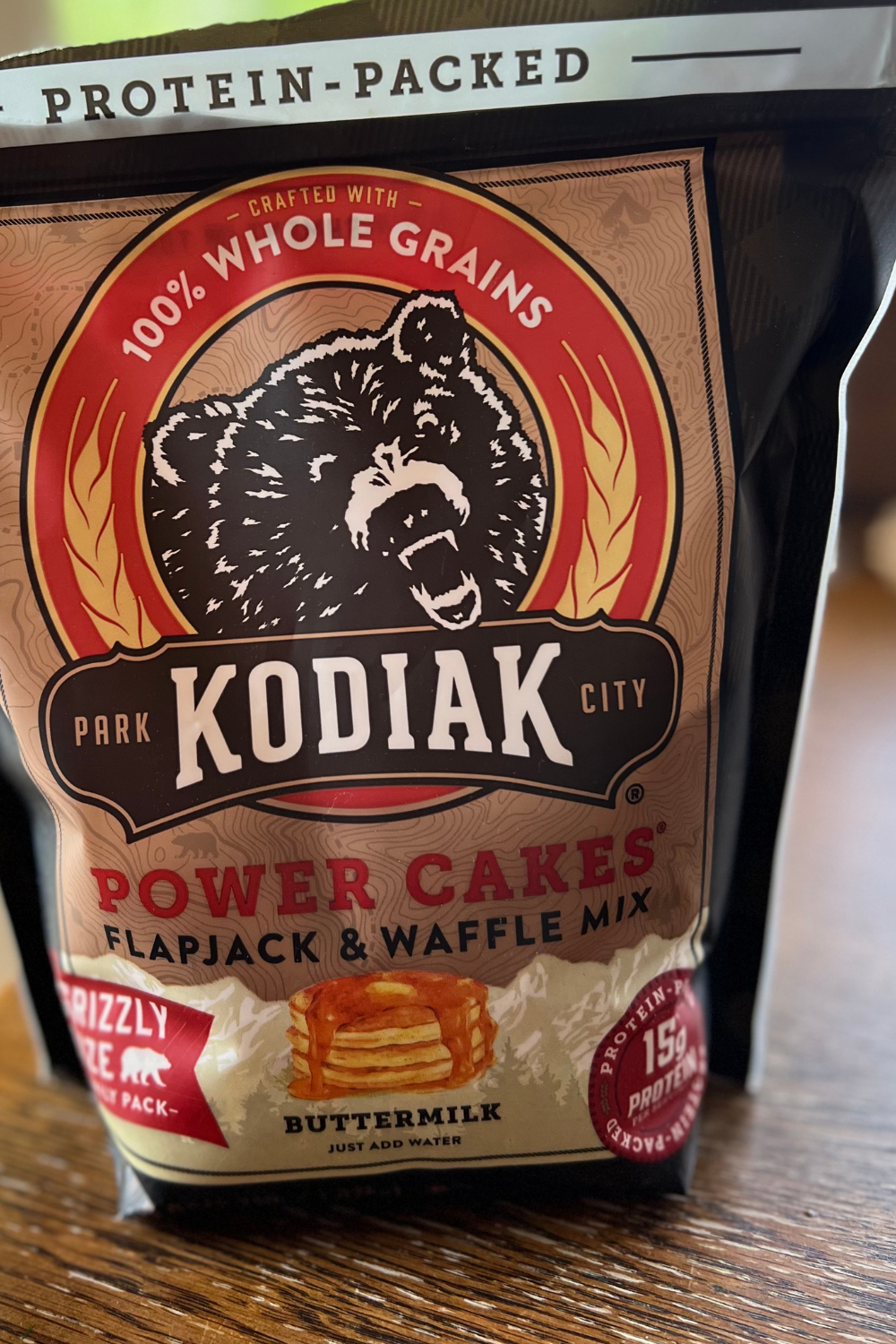 A bag of Kodiak Cakes Power Cakes Flapjack & Waffle Mix, Buttermilk flavor, with a bear logo and "100% Whole Grains" and "Protein-Packed" labels on the packaging.