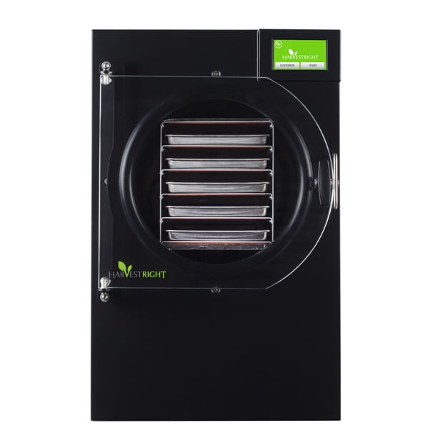 Front view of a black Harvest Right freeze dryer with a clear door revealing five metal trays inside and a green digital display on the top right corner. Save more on your Harvest Right purchase with a coupon code.