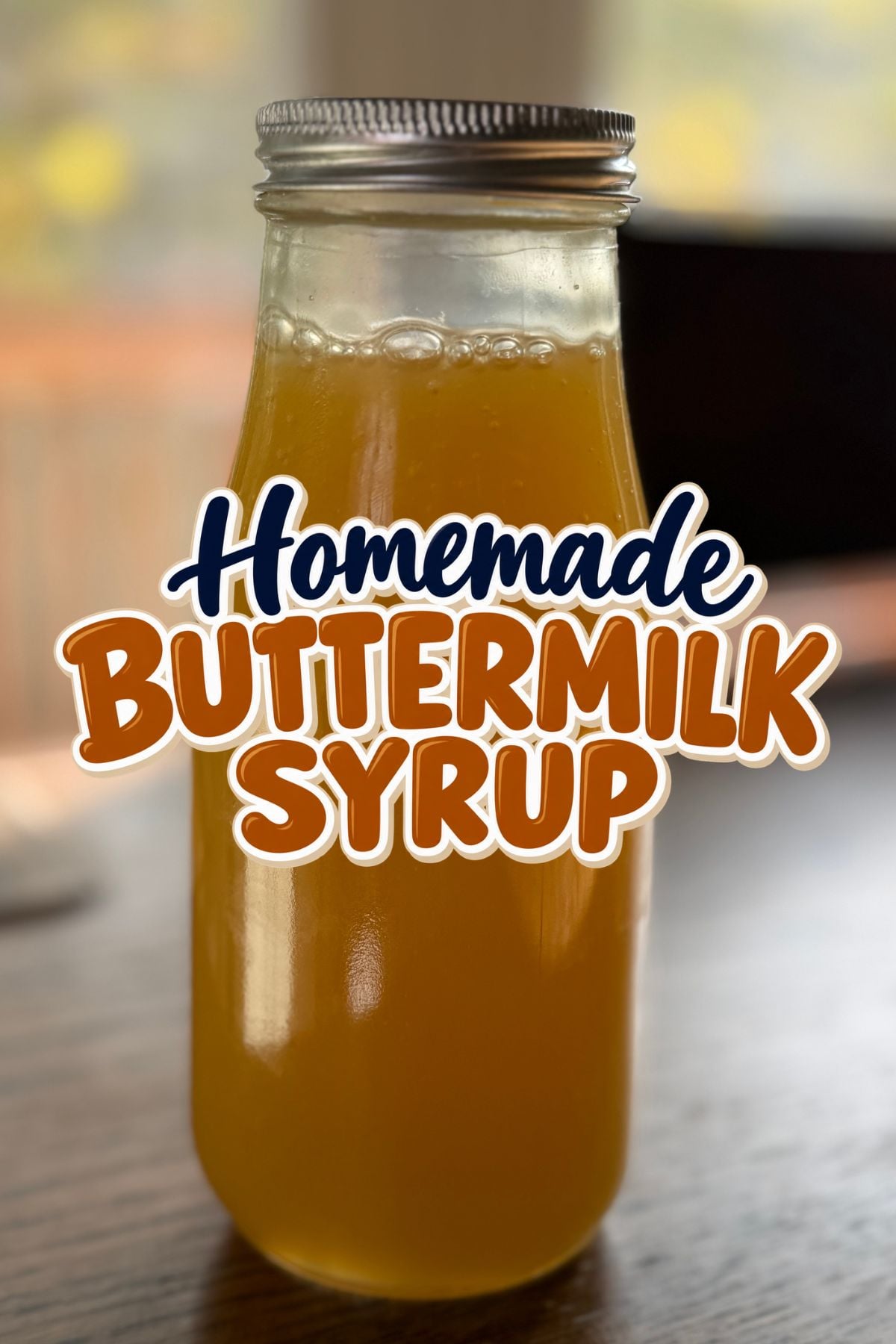 Glass jar filled with golden homemade buttermilk syrup, featuring a silver lid and a bold “Homemade Buttermilk Syrup” title overlay in navy blue and caramel-colored lettering.
